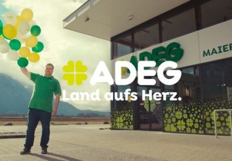 Requisite Werbung "130 Jahre ADEG", Mann mit Luftballonen in der Hand steht vor seinem Kauhaus