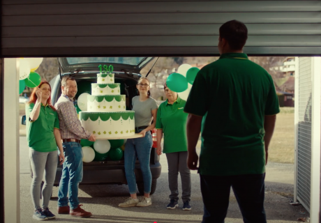 Requisite Werbung "130 Jahre ADEG", Mann vor sich öffnendem Garagentor wird von mehreren Leuten mit riesiger Torte überrascht