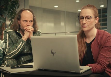 Ausstattung und Requisite Werbung "Datev", Mann mit grünem Jogginganzug schaut gespannt auf eine Frau, die etwas am Laptop recherchiert