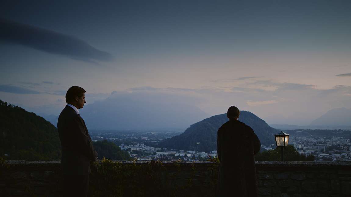 Szenenbild und Kostümbild Film – Filmstill aus der Dokumentation „Virginia“, zwei elegante Personen vor einem Panorama über die Stadt Salzburg