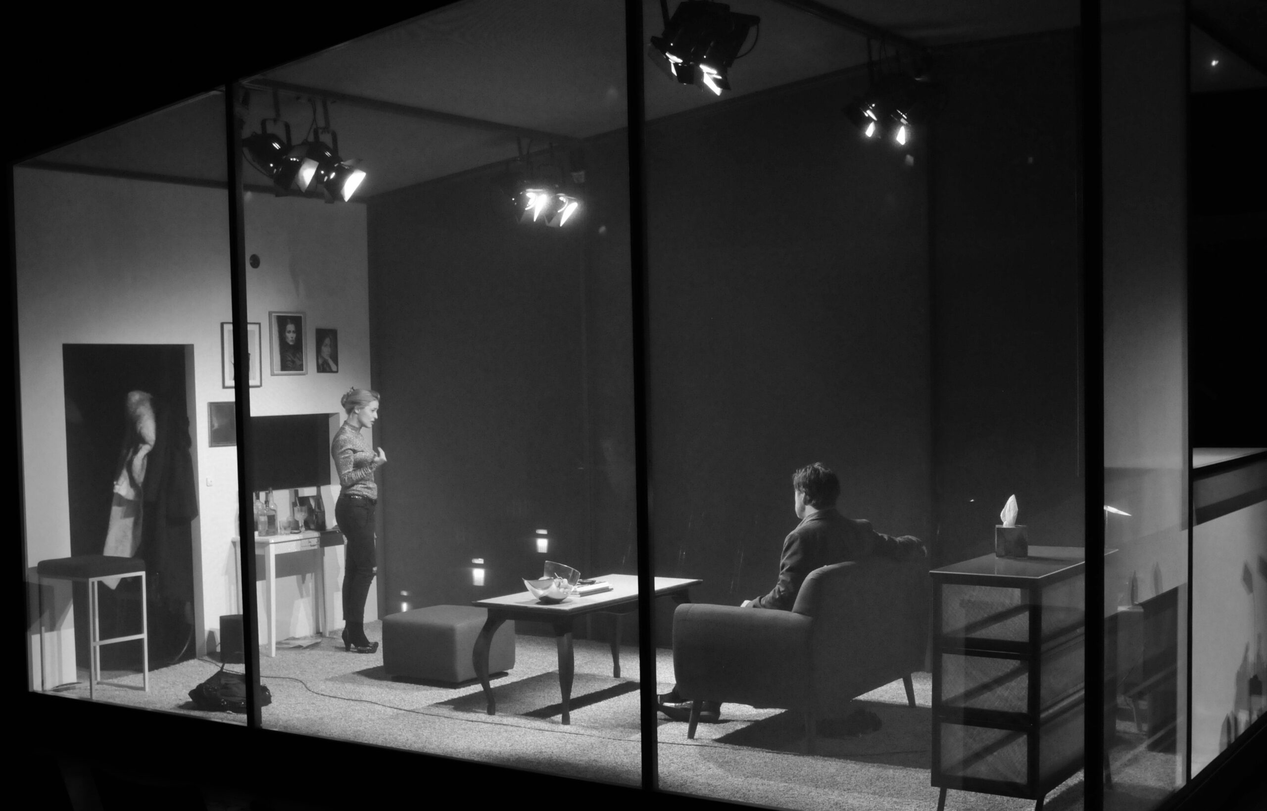 Bühnenbild und Kostümbild Theater – Theaterstück „Das Interview", Blick auf einen durch transparente Wände abgeschlossenen Bühnenraum, in dem sich ein Wohnzimmer befindet.