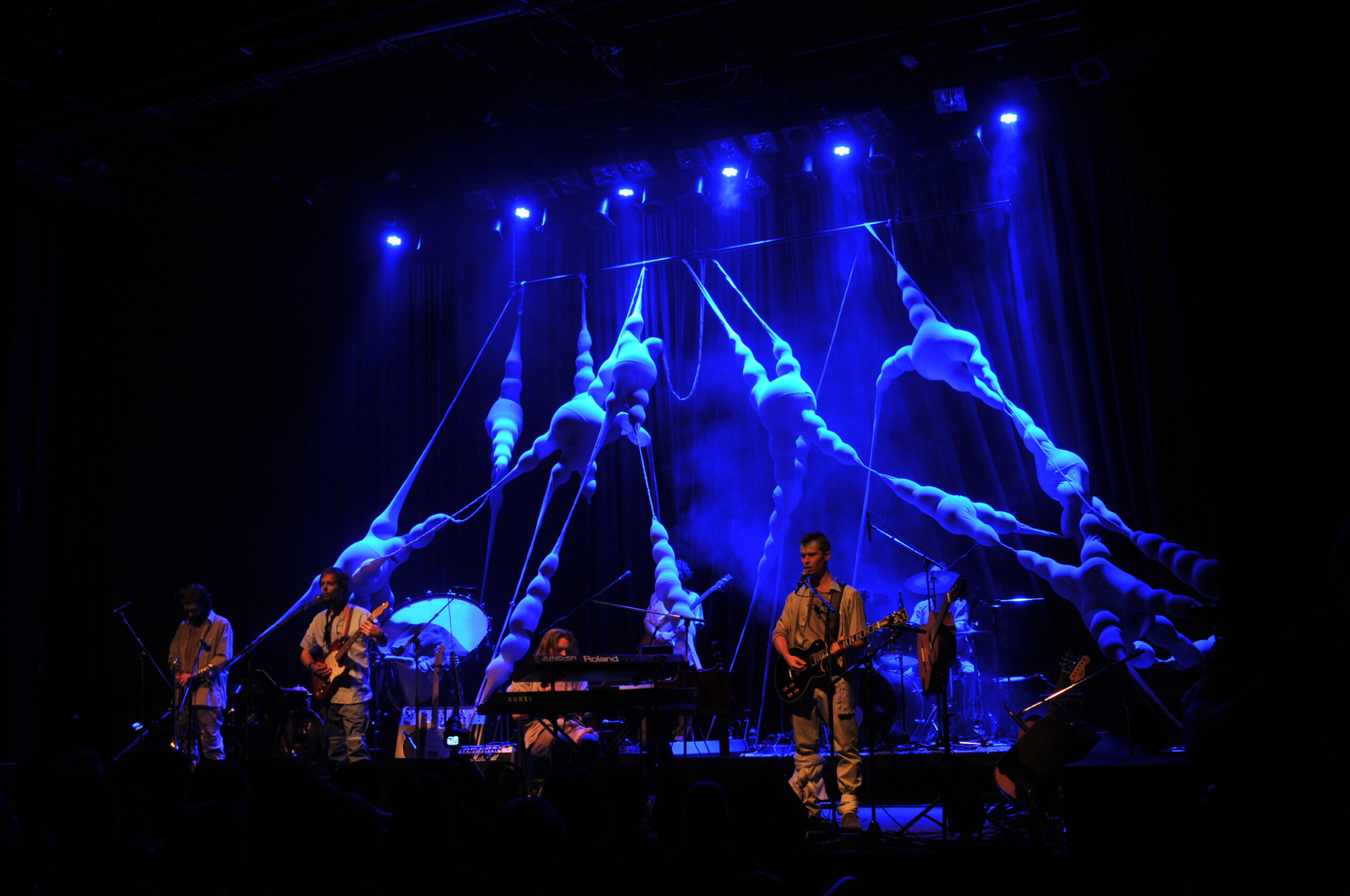 Bühnenbild und Kostümbild Konzert „Krásná Hora“, beleuchtete, organische Bühneninstallation, die sich quer über die Bühne spannt, im Vordergrund die Band Blank Manuskript