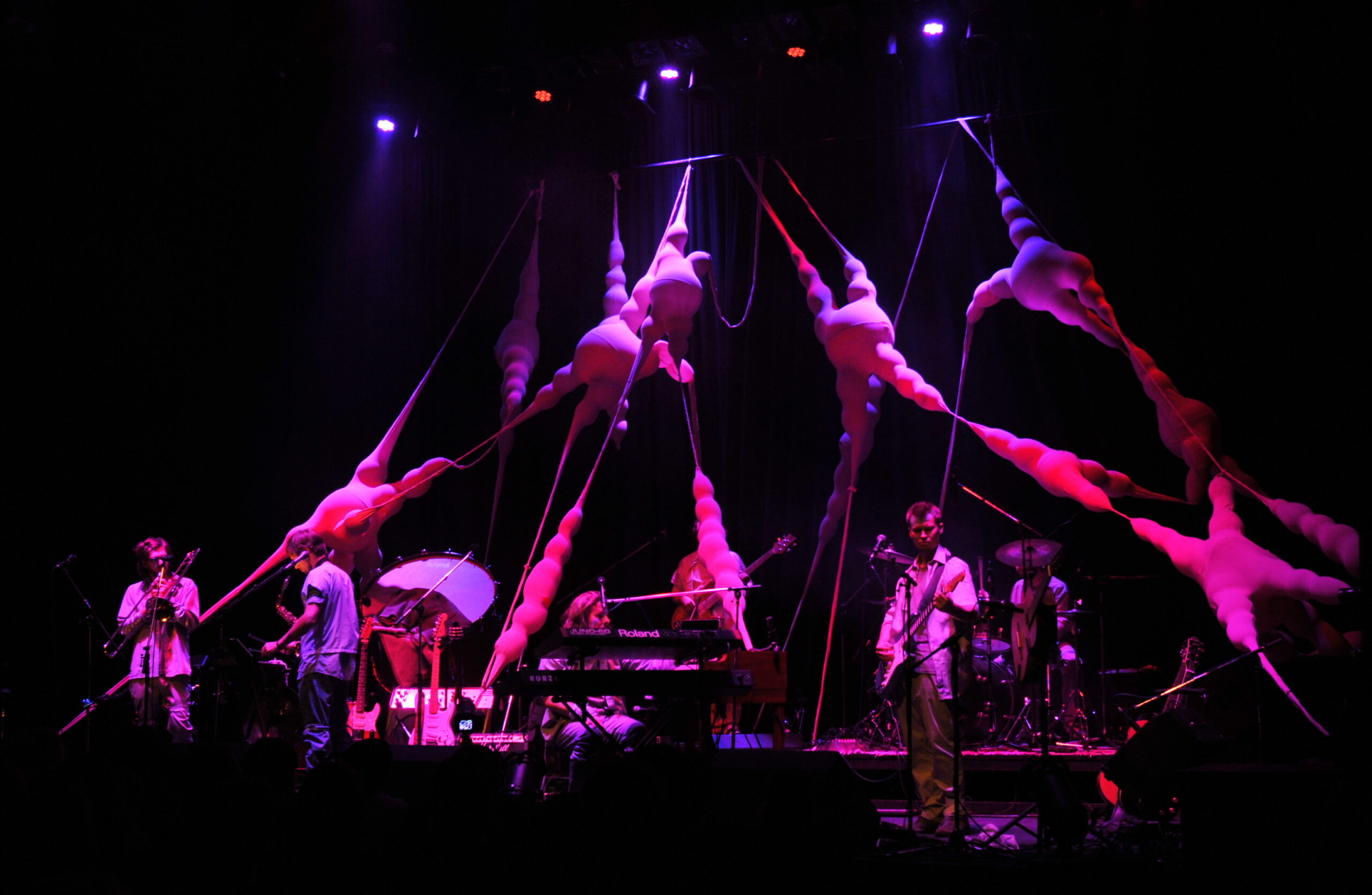 Rosa beleuchtete, organische Bühneninstallation, die sich quer über die Bühne spannt, im Vordergrund ein Musiker