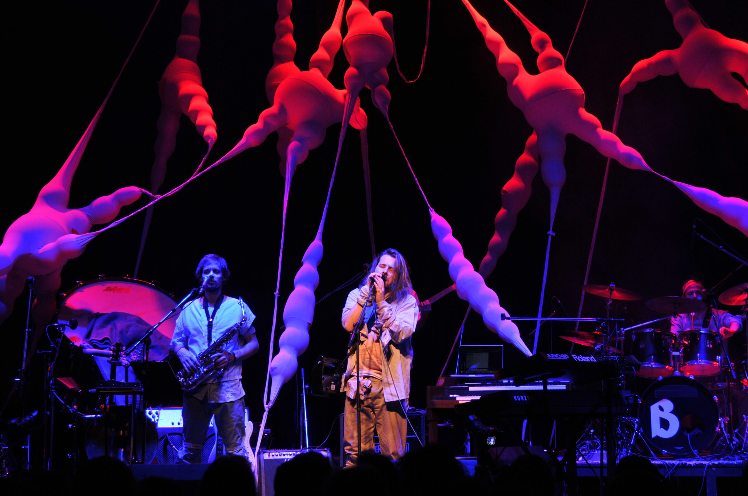 Bühnenbild und Kostümbild Konzert „Krásná Hora“, beleuchtete, organische Bühneninstallation, die sich quer über die Bühne spannt, im Vordergrund ein Saxophon-Spieler und ein Sänger