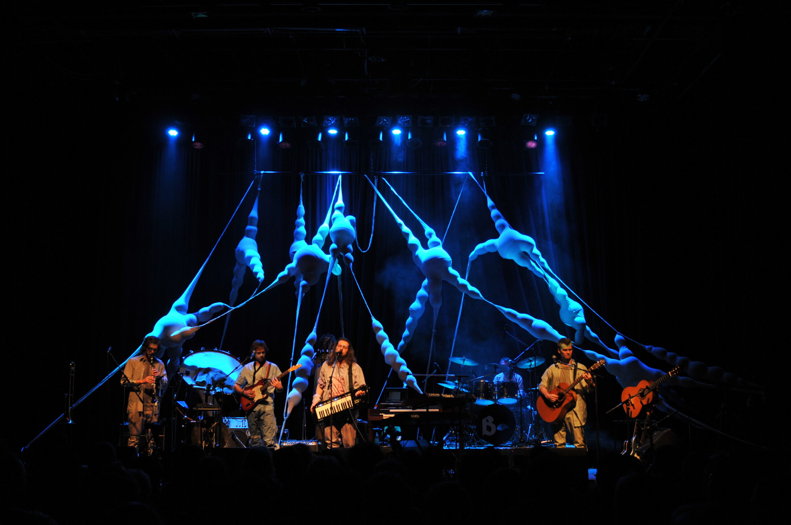 Organische Installation, die sich quer über die Bühne spannt, im Vordergrund eine Band mit fünf Musikern