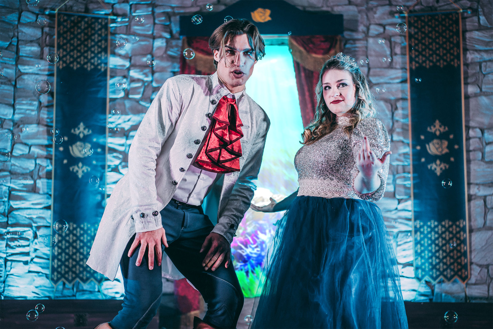 Bühnenbild und Kostümbild Theater – Musical „Magical Singalong“, Prinz und Prinzessin blicken ins Publikum, Seifenblasen und Schlossbanner im Hintergrund