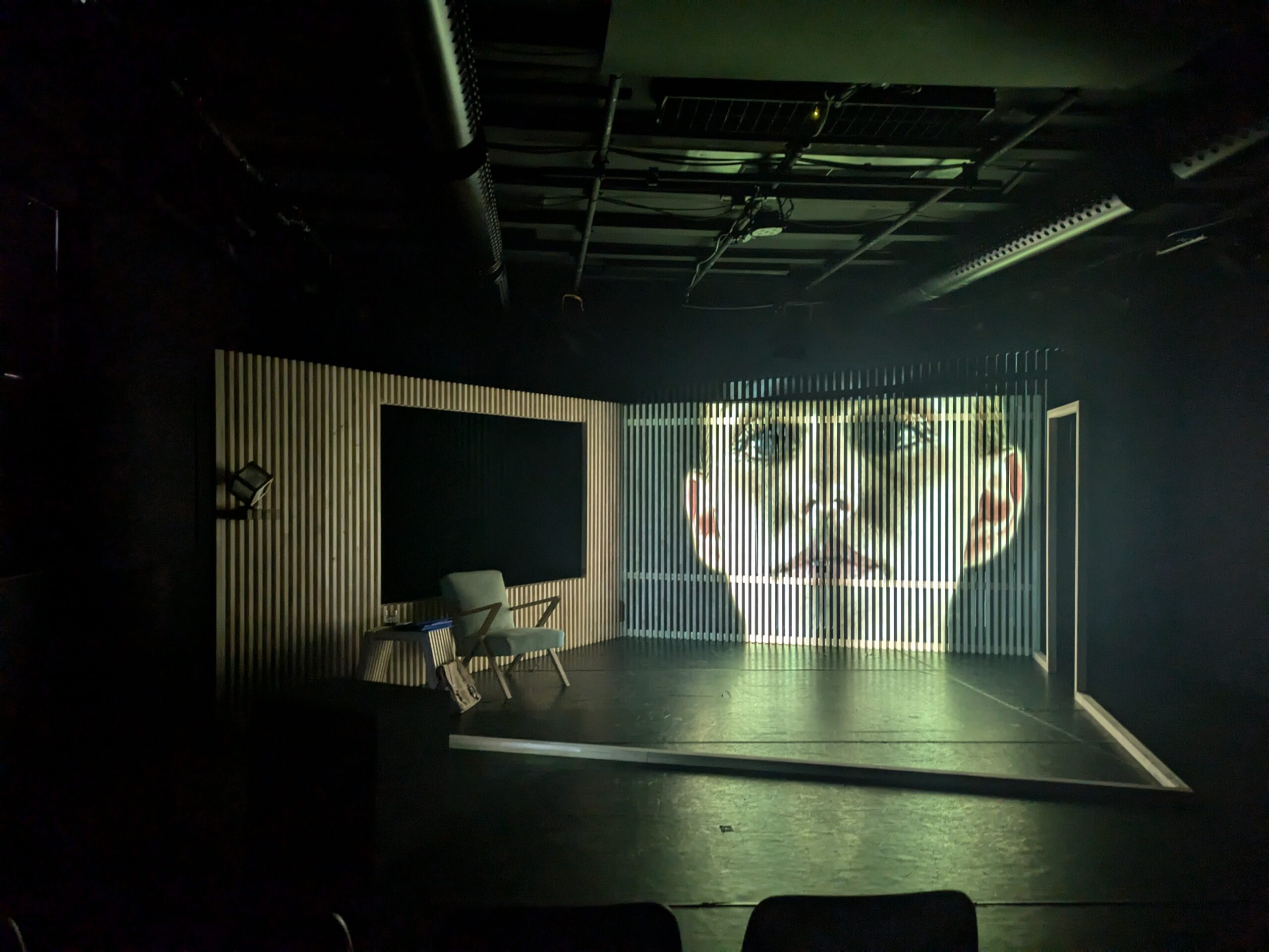 Ein reduzierter Bühnenraum mit einer Hinterwand aus Latten, auf die das Gesicht einer jungen Frau projiziert ist
