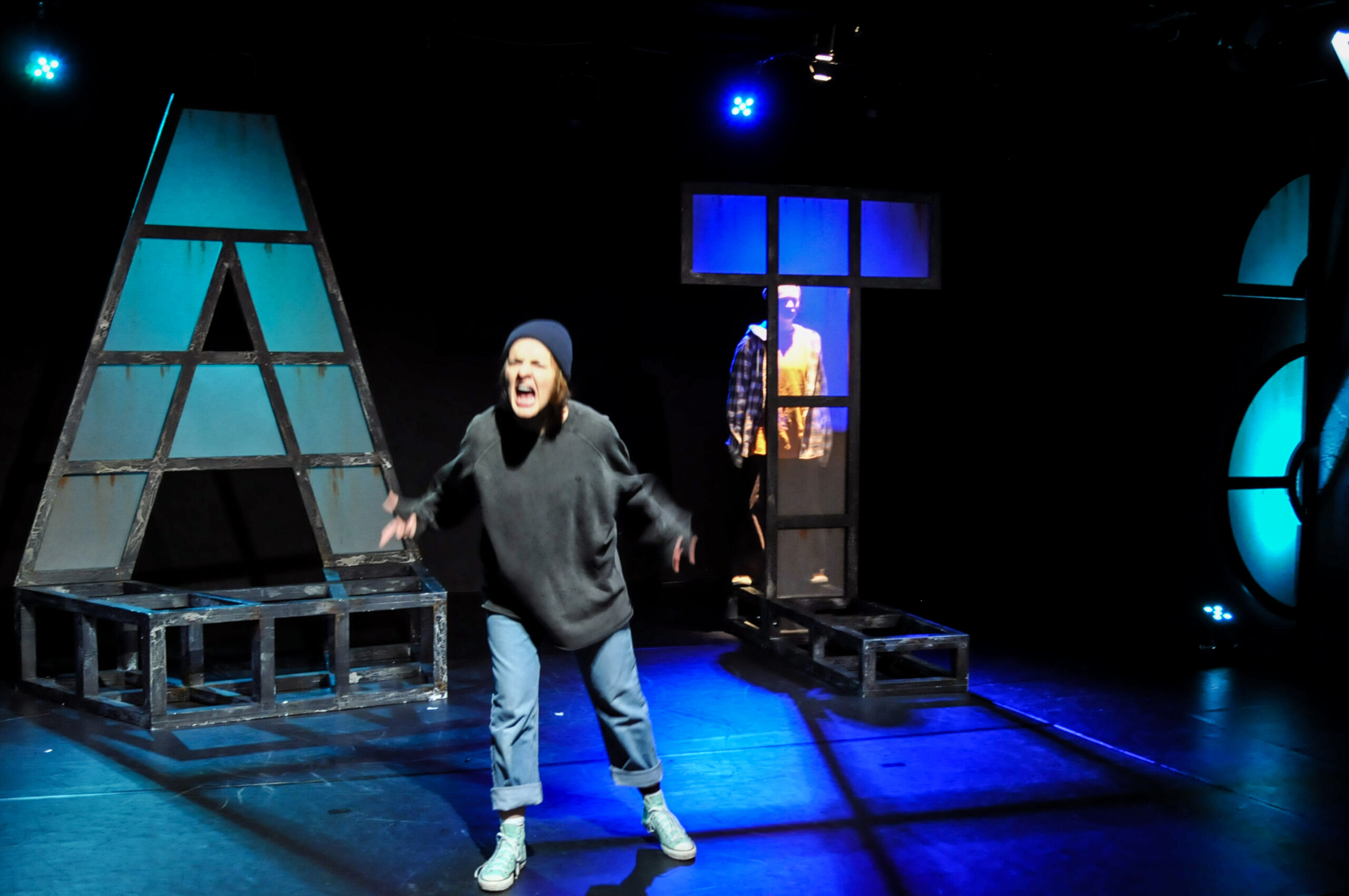 Bühnenbild und Kostümbild Theater – Theaterstück „Das Gesetz der Schwerkraft“, eine junge Frau schreit vor einer Kulisse aus Buchstaben