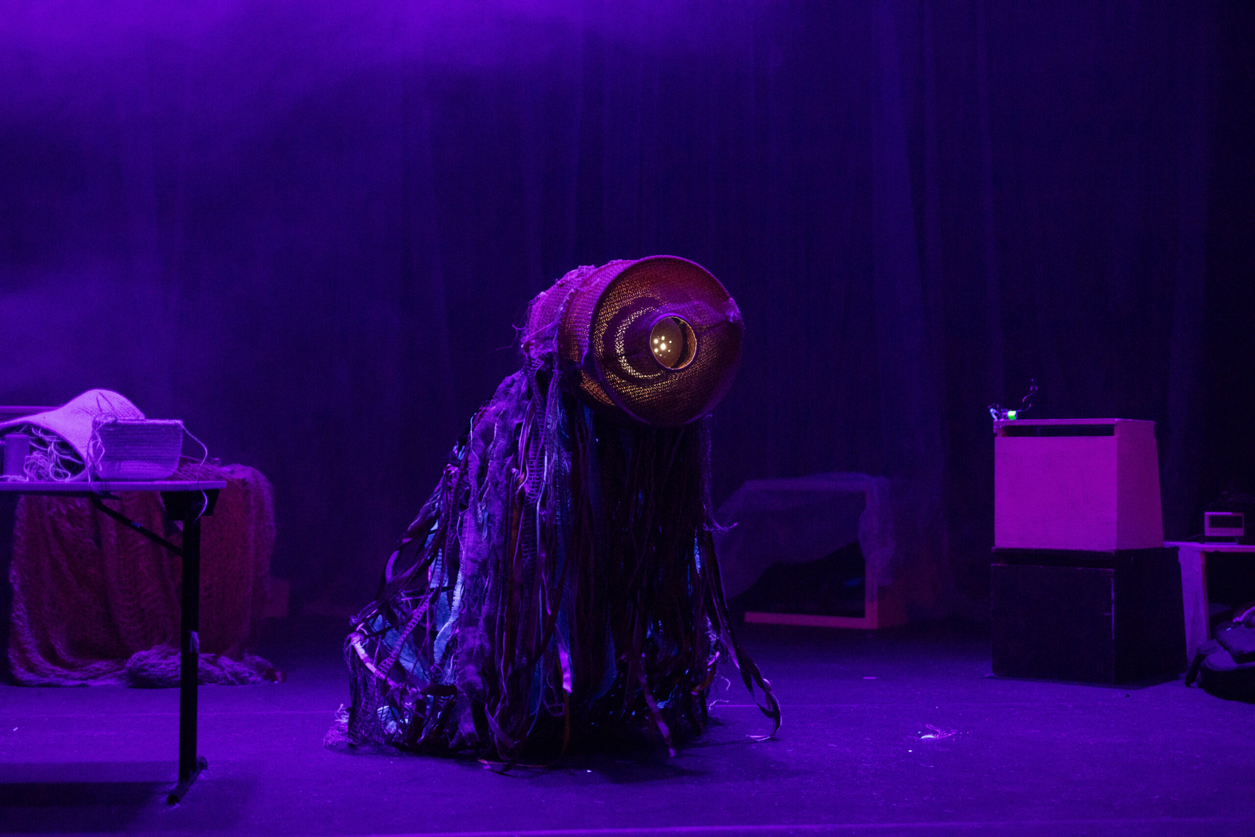 Ein seltsames Fastnachts-Wesen mit langen Fäden und einem leuchtenden Kopf in einem dystopischen, in Lila getauchten Raum