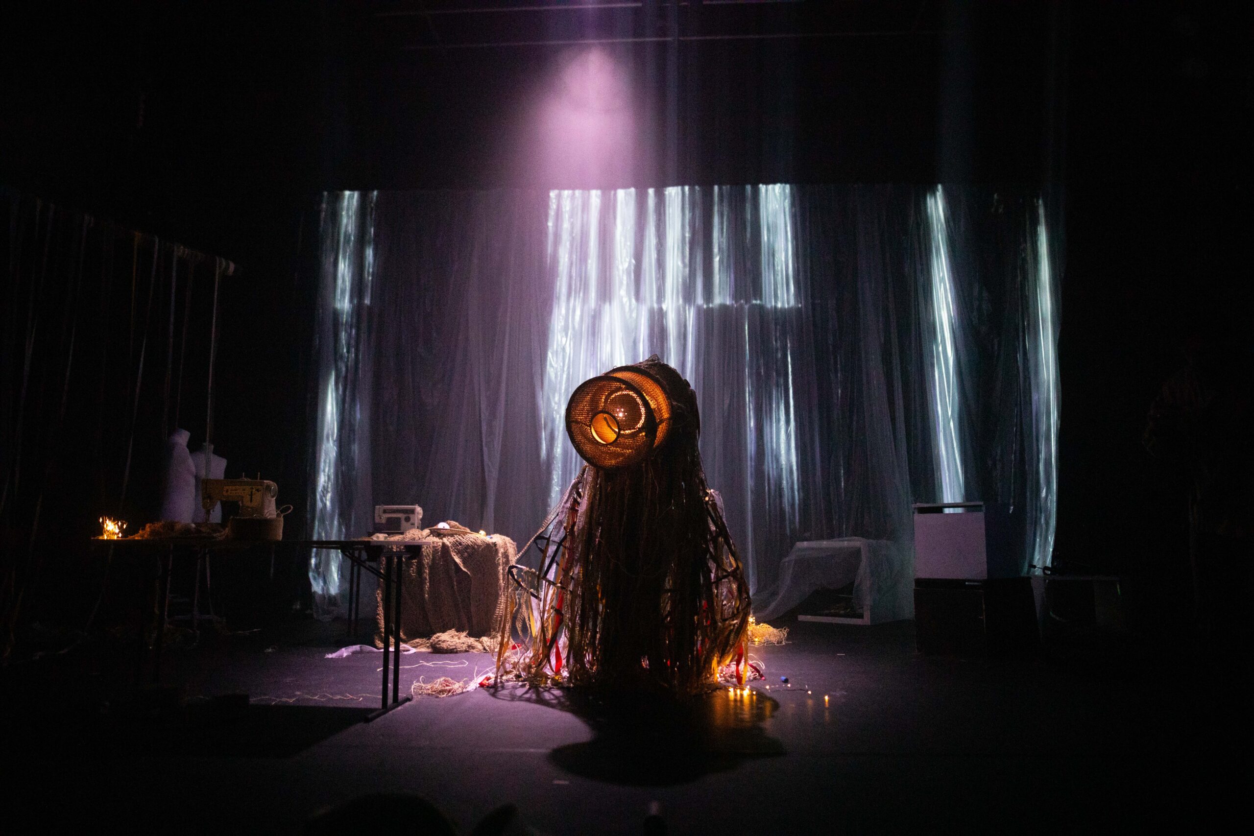 Bühnenbild und Kostümbild Theater – Tanztheater „The Collapse“, ein seltsames Wesen mit langen Fäden am ganzen Körper steht in der Mitte eines dunklen, dystopischen Bühnenraumes