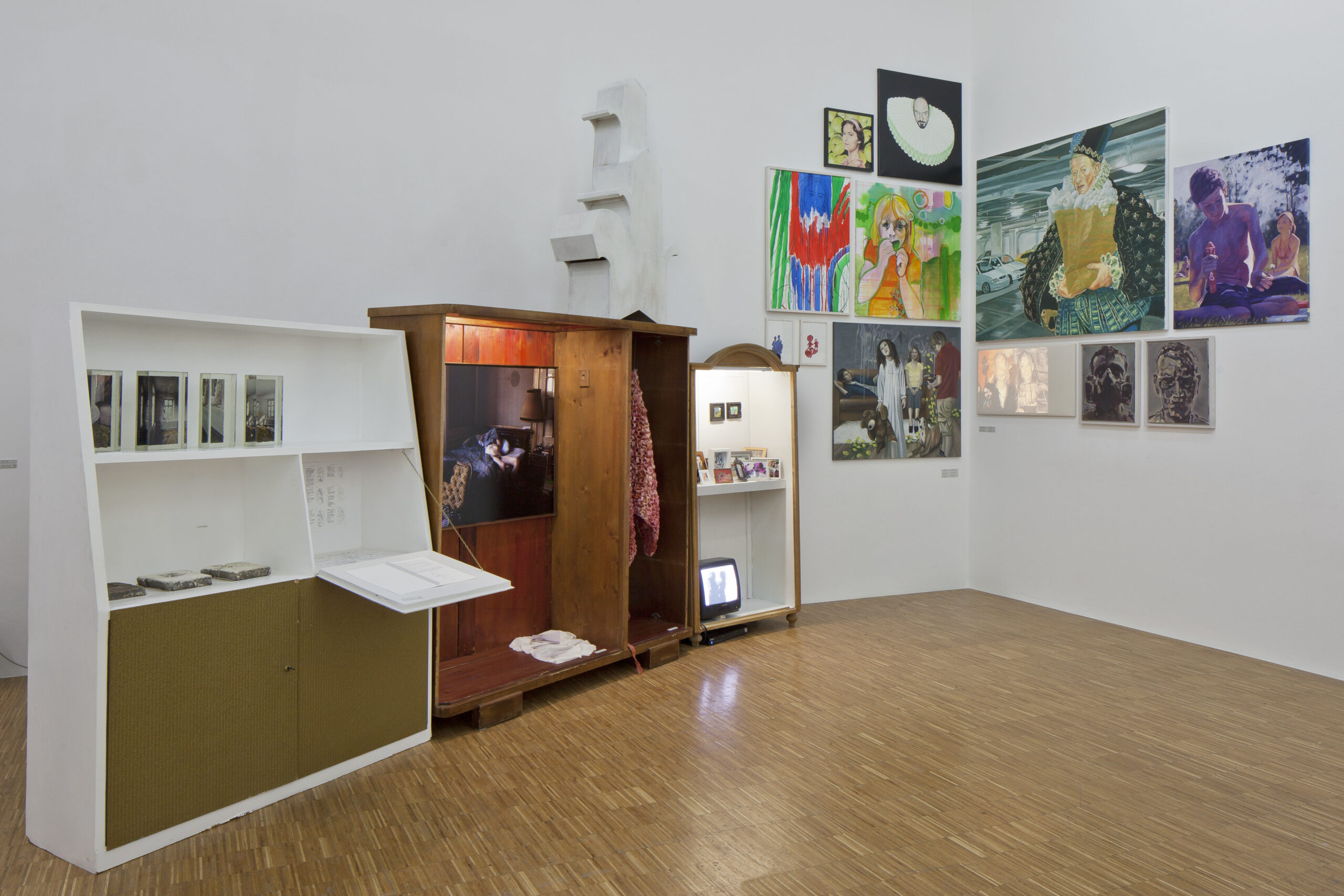 Ein Ausstellungsraum wie eine Wunderkammer: alte Schränke, in denen sich verschiedene Kunstwerke befinden, und Bilder an der Wand