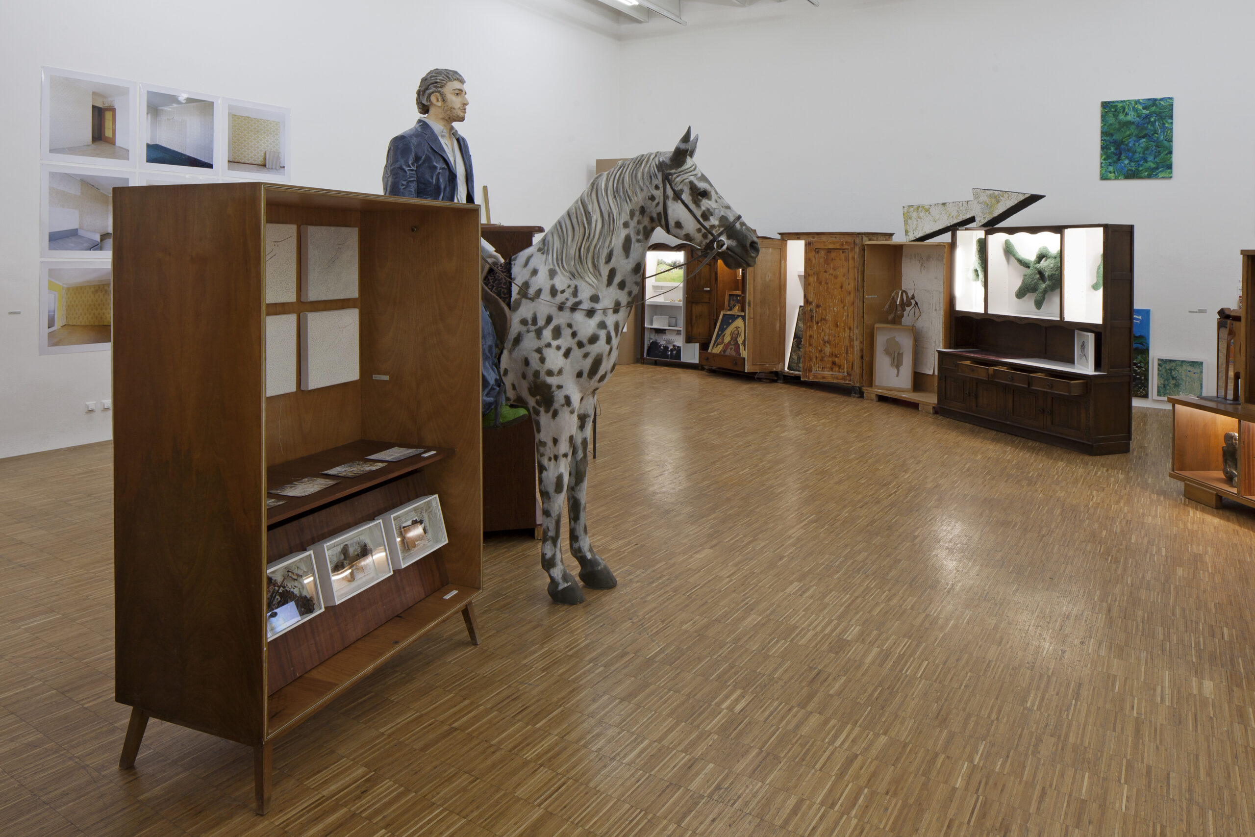 Ein Ausstellungsraum wie eine Wunderkammer: ein riesiges Pferd mit Reiter und alte Schränke, in denen sich verschiedene Kunstwerke befinden